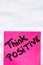 Think positive handwriting text close up isolated on pink paper with copy space. Writing text on memo post reminder