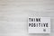 `Think positive` words on a lightbox on a white wooden background, top view. Overhead, from above, flat lay. Copy space