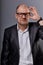 Thinking bald business man looking serious in eyeglasses in suit on grey background. Closeup