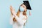 Thinking girl graduate in a medical mask, student in a graduation hat thinks and looks to the side on a blue background