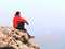 Thinking man sit on rock. Man on view point of exposed peak watching to misty far distance.