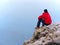 Thinking man sit on rock. Man on view point of exposed peak watching to misty far distance.