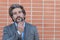 Thinking mature bearded man in a suit with touching his beard looking away. Desaturated portrait over brick wall background