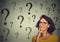 Thinking young business woman in glasses looking up at many question marks