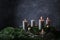 Third advent with three burning candles on fir branches with Christmas decoration against a dark grey background, copy space