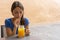 Thirst Teen smiling by the pleasure of a refreshing orange juice. Girlfriend sitting relaxing drinking a smoothie by plastic straw