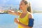 Thirsty fitness woman opens bottle of water after training outdoor. Fit woman using smartphone fitness app on armband as activity