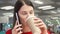 Thirsty girl drinking coffee from paper cup at fast food restaurant on food court. Talking on the phone