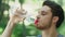 Thirsty man drinking water from bottle in summer park. Portrait of sport man