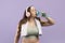 Thirsty millennial european plus size woman in sportswear with towel in headphones drinks water from bottle