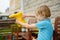 Thoroughly soaked preschooler boy pours water out of a yellow rubber boot after running and jumping on puddle in the rain. Child