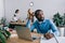 thoughtful african american businessman sitting at table and coworkers working behind in modern