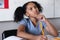 Thoughtful biracial elementary girl with hand on chin looking up while studying at desk in classroom