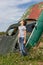 Thoughtful caucasian teenage standing on the grass in countyside in summer day with serious face expression, a retro car is on