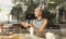 Thoughtful caucasian woman holding mobile phone while looking through the coffee shop window during coffee break.