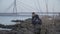 Thoughtful Caucasian young man sitting on riverbank and throwing rocks in water. Portrait of sad handsome guy in