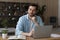 Thoughtful dreamy businessman in glasses sitting at desk with laptop