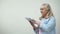 Thoughtful elderly lady scrolling screen on tablet, online banking application