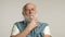 Thoughtful elderly man with gray beard, white tee, denim vest, white background