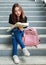 Thoughtful ethnic female traveler sitting on stairs with paper map and looking for tourist destination. City life travel and