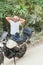 Thoughtful ethnic young man in casual clothes and cap standing near a modern motorcycle with his hands behind his head and looking