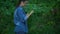 Thoughtful female examining infected tree leaves, plastic garbage on ground