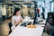 Thoughtful female student reading textbook and using computer while studying in library