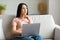 Thoughtful Freelancer Woman At Laptop Thinking Sitting On Sofa Indoors