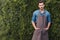 Thoughtful gardener in apron looking at camera while standing in garden