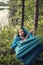 Thoughtful girl lying in a hammock and strumming the guitar melody, a summer evening in the woods on a background of lake.