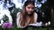 Thoughtful girl reading book while lying on blanket in green park