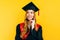 A thoughtful, graduate in a master`s dress, on a yellow background. Concept of the graduation ceremony