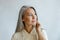 Thoughtful grey haired woman in stylish shirt looks aside on light background