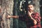 Thoughtful handsome man in red shirt touching his beard. Young hiker with tattoo on his arm relaxing in woods