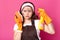 Thoughtful impressed housewife looks at dirty sponge, looks shocked, posing  over pink background in studio. Exhausted