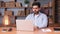 Thoughtful Indian businessman works on a laptop at a modern office desk.