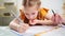 A thoughtful little schoolgirl does her homework, nervous and biting nails