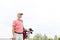 Thoughtful middle-aged golfer looking away while carrying bag against clear sky