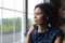 Thoughtful millennial african american woman standing near window.