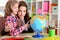 Thoughtful mother and daughter sitting at table with globe