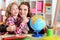 Thoughtful mother and daughter sitting at table with globe