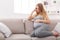 Thoughtful pregnant woman sitting on sofa