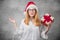 Thoughtful Santa woman with christmas gift isolated on gray background. Young girl wearing red santa hat and holding present box