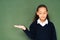 thoughtful, sceptical schoolgirl pointing with hand at green chalkboard .