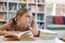 Thoughtful school girl reading book in library