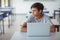 Thoughtful schoolboy sitting with laptop in classroom