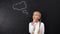 Thoughtful schoolgirl touching chin and looking to sides idea sign on blackboard