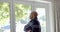 Thoughtful senior biracial man looking through window at home, slow motion