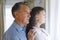 Thoughtful senior caucasian couple standing next to window, embracing