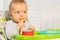 Thoughtful toddler boy sit in highchair with spoon